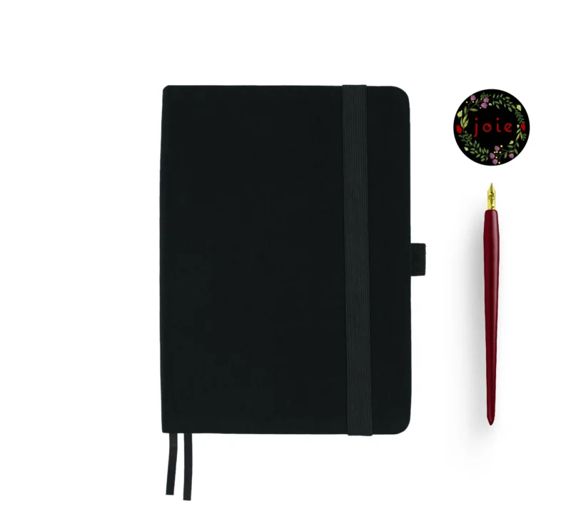 Black fabric-covered notebook with rounded corners, matching black elastic band, pen loop, and dual ribbon bookmarks, displayed with a red fountain pen and a floral 'joie' logo