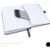 Dark grey leather-textured fabric notebook with rounded corners, matching elastic band, pen loop, and dual ribbon bookmarks, shown with a green and yellow fountain pen illustration and a floral 'joie' logo