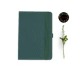 Deep green fabric-covered notebook with rounded corners, matching elastic band, pen loop, and dual ribbon bookmarks, shown with a white flower and a floral 'joie' logo